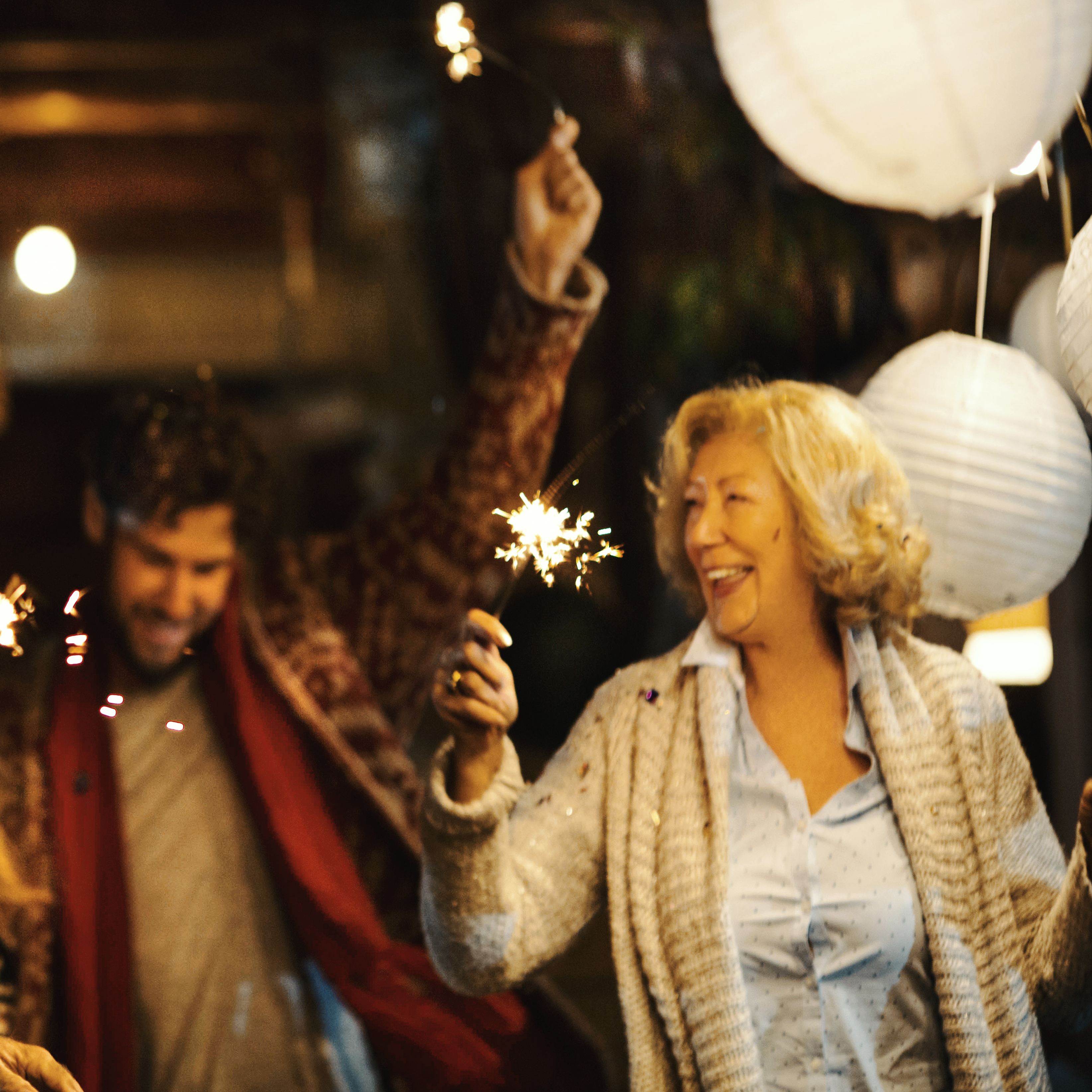 An older woman and her son celebrate New Year’s with sparklers.